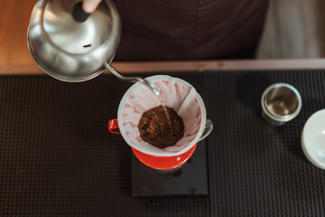 Top view barista holding kettle pour hot water over the coffee powder. Making filter coffee. Drip...