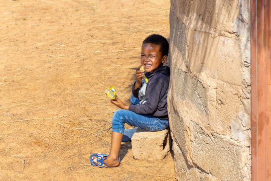 hungry african child eating biscuits , african village homestead yard with shack