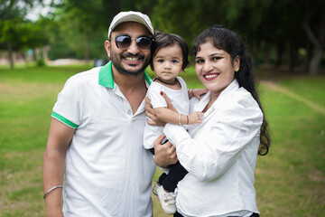 Happy Young indian parents with their cute little adorable daughter enjoying in park or garden. lifestyle concept.