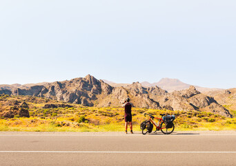 Caucasian male person takes photograph of scenic mountains by bicycle on highway on vacation in...