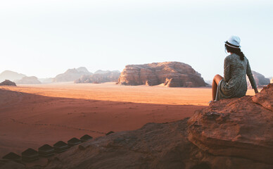 Fototapeta na wymiar Woman tourist in dress sit on cliff at viewpoint on sunset in Wadi Rum desert - valley Wadi Saabit. Jordan explore concept
