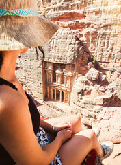 Caucasian woman traveler sit on viewpoint in Petra ancient city look Treasury or Al-khazneh, famous...