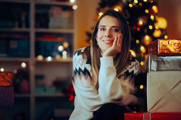 Happy Woman Smiling in front of a Christmas Tree. Cheerful girl waiting for Xmas celebration at home feeling serene
