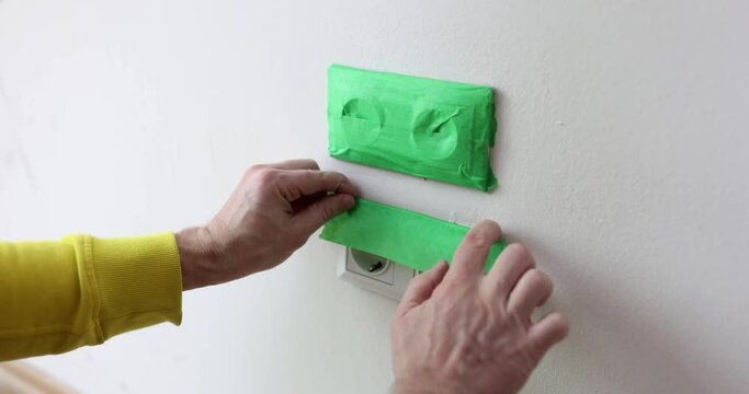 Builder sealing sockets with green masking tape before painting walls closeup 4k movie slow motion. Careful construction work concept