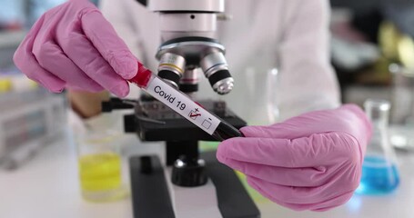 Laboratory technician wearing medical gloves holds positive test for covid 19. Scientist in a biolaboratory examines patient with covid 19 coronavirus using microscope