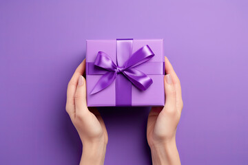 top view hand holding a purple gift box with ribbon on a violet background