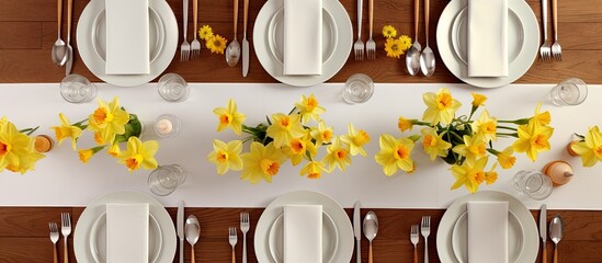 Bird's eye view of table setting with white plates, cutlery, yellow daffodils, wooden table, and chairs on tiled floor.