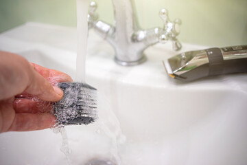 Washing the nozzle for an electric clipper under running water.Disinfection of the instrument after the visitor. Cleaning the shaving machine at home.