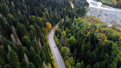 a road in the mountains in an autumn multicolored forest shot from above on a copter - Powered by Adobe