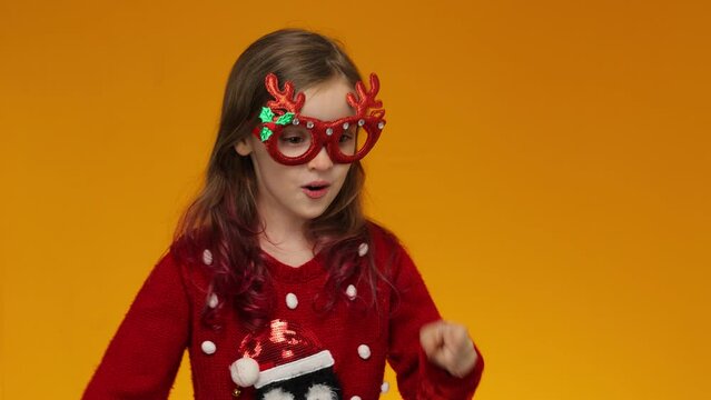 The child in a red Christmas sweater and deer horns on her head points at the fictional inscriptions with his finger. Yellow background