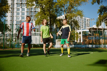 Smiling male friends football player walking among on soccer field