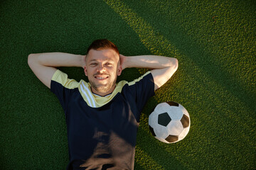 Happy smiling restful football player lying on green field grass