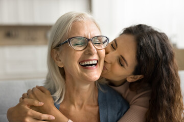Happy loving adult daughter kissing cheerful laughing mature mum with love, gratitude, congratulating on mothers day, enjoying family meeting, visit, friendship, leisure time - obrazy, fototapety, plakaty