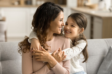 Happy pretty loving little kid girl hugging positive mom, playing with parent at home. Beautiful...