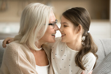 Happy senior grandma and cute grandkid girl hugging with faces touch, laughing, enjoying leisure, playtime, family meeting, relationship. Granny hugging grandchild with love, affection - obrazy, fototapety, plakaty