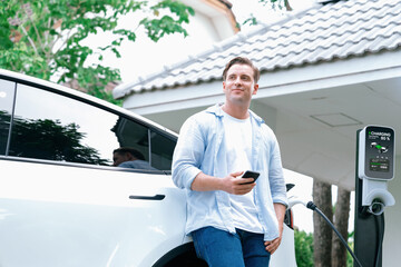 Modern eco-friendly man recharging electric vehicle from home EV charging station. Innovative EV...