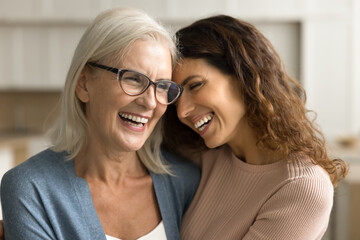 Cheerful loving senior mom in glasses and pretty adult daughter woman hugging with emotional heads touch, laughing with closed eyes, smiling, enjoying talk, family connection, closeness