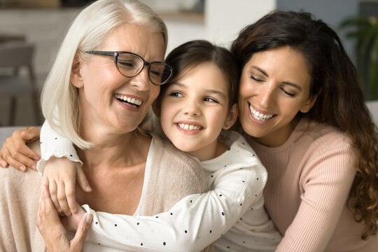 Happy girls and women of three family generations hugging with love, tenderness at home, feeling close family relations, bonding, smiling, laughing. Grandma, mom and kid girl meeting on mothers day