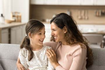 Obraz na płótnie Canvas Excited pretty mother and positive little daughter girl having fun on home sofa, talking, laughing, feeling closeness, trust. Happy mom cuddling child on couch, enjoying family leisure