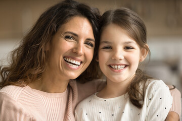 Positive beautiful mom and happy tween kid girl looking at camera, smiling, showing white healthy...