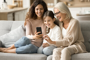 Happy kid, mom and grandma enjoying domestic online communication, taking selfie on mobile phone,...