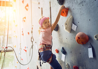 Fototapeta premium A strong baby climber climbs an artificial wall with colorful grips and ropes.