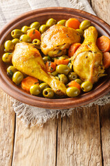 Tajine Zitoune is an Algerian stew dish that consists of chicken cooked with carrots and green olives using north African spices close-up on wooden table. Vertical