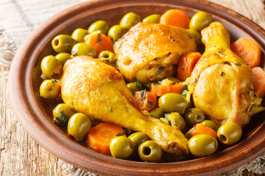 Tajine zitoun is a traditional Algerian dish made with a combination of chicken pieces, olives, onions, carrots close-up on wooden table. Horizontal