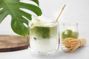Glass of tasty iced matcha latte, leaf and bamboo whisk on white table, closeup