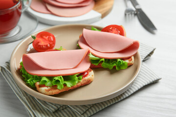 Plate of tasty sandwiches with boiled sausage, tomato and lettuce on white wooden table, closeup © New Africa