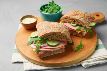 Tasty sandwiches with boiled sausage, cucumber, arugula and sauce on grey table, closeup