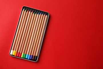 Box with many colorful pastel pencils on red background, top view and space for text. Drawing supplies