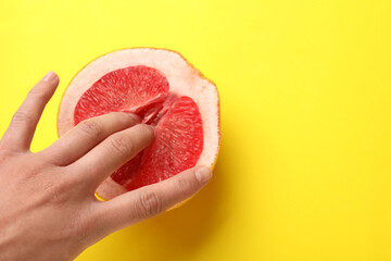 Woman touching half of grapefruit on yellow background, top view and space for text. Sex concept - obrazy, fototapety, plakaty