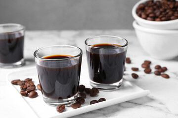 Glasses of coffee liqueur and beans on white marble table, closeup