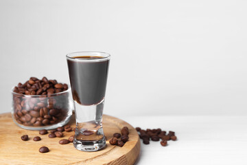 Shot glass of coffee liqueur and beans on white table, space for text
