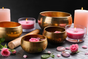 Tibetan singing bowls with beautiful rose flowers, mallet and burning candles on gray table