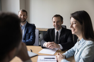 Joyful teammates take part in morning briefing, laugh, share ideas, enjoy creative cooperation, friendly relations and successful teamwork gathered together in office board room. Business, deal, fun