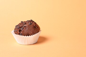 Tasty chocolate muffin on pale orange background, space for text