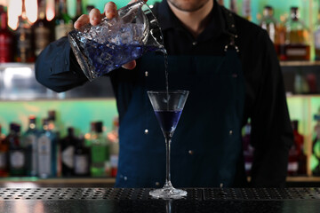 Bartender making fresh alcoholic cocktail at counter in bar, closeup
