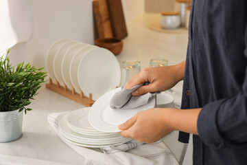 Woman wiping plate with towel in kitchen, closeup