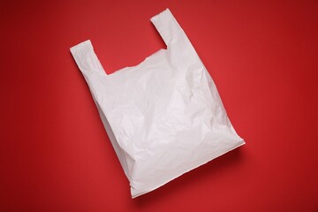 One empty plastic bag on red background, top view