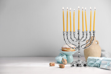 Hanukkah celebration. Menorah with burning candles, dreidels and gift boxes on white table, space...