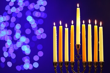 Hanukkah celebration. Menorah with burning candles on blue background with blurred lights, space for text