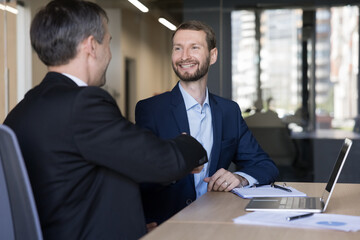 Young smiling businessman, sales manager shakes hands greeting company client start or finish formal meeting in office, feel satisfied with successful partnership, accomplish negotiation, make deal