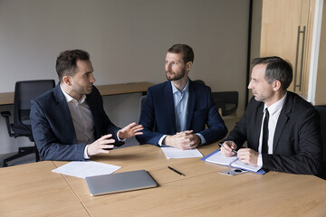 Mature and millennial colleagues, business partners engaged in formal negotiations, planning joint project and future partnership sit at desk in company conference room. Cooperation, deal discussion
