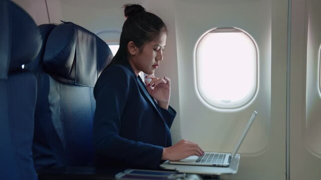 Asian businesswoman working on her laptop while traveling by plane to attend meetings or gather information for her business. Stay productive on the go