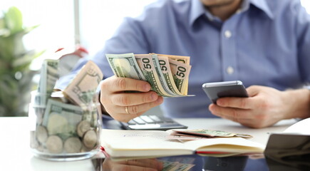 Male hand holding pack of banknotes and cellphone making some calculation planning his future...