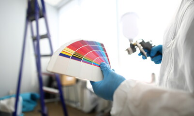 Hands of workman holding airbrush and colorful fantail picking wall tone to paint closeup