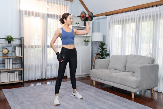 Vigorous energetic woman doing dumbbell weight lifting exercise at home. Young athletic asian woman strength and endurance training session as home workout routine. © Summit Art Creations