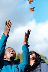 Two funny mature women playing with autumn leaves outdoors.